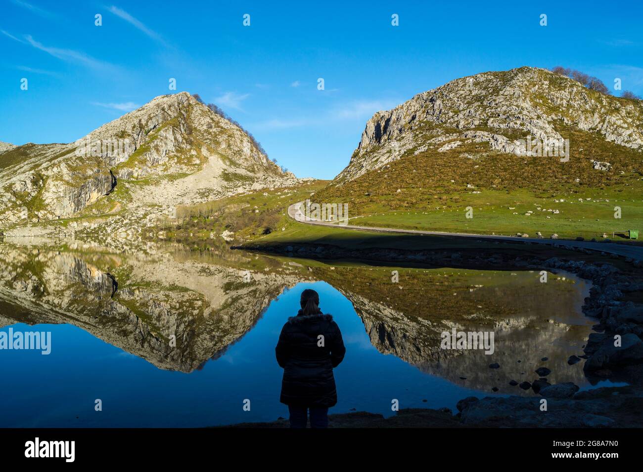 Silhouette of a woman observing the reflection of the mountains in Lake Enol.The photograph is taken at sunrise in the Lakes of Covadonga, Asturias, S Stock Photo
