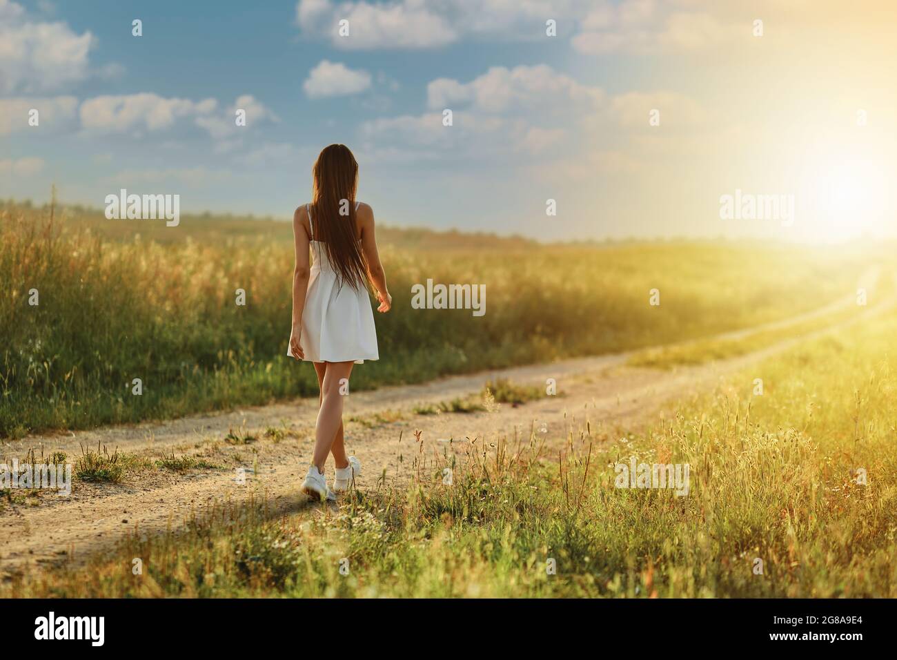 Rear view of a woman walking along country road in the meadow during ...