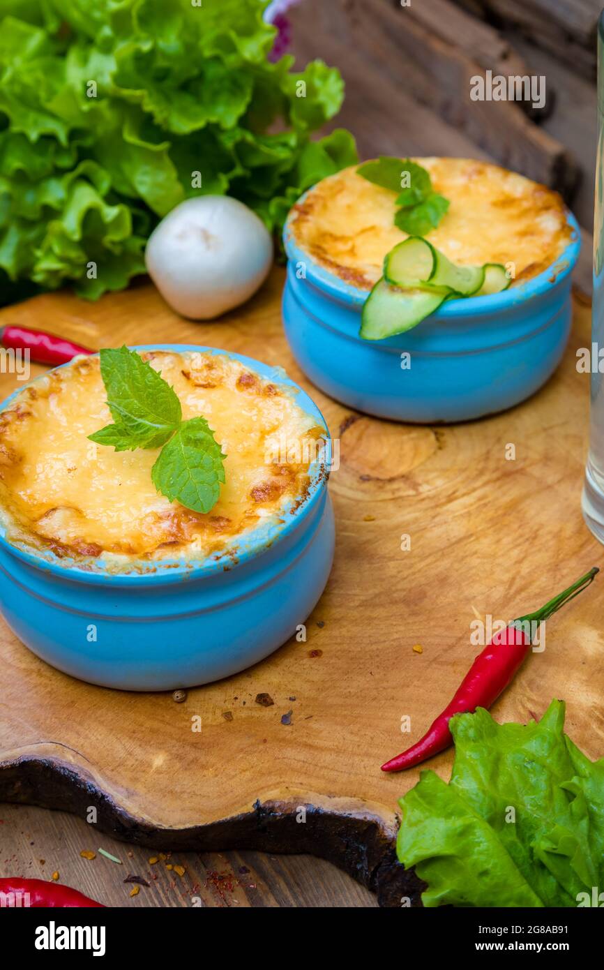 Pots with mushroom julienne on a wooden board, decorated with herbs. Julienne in cocotte with yellow cheese crust. Stock Photo