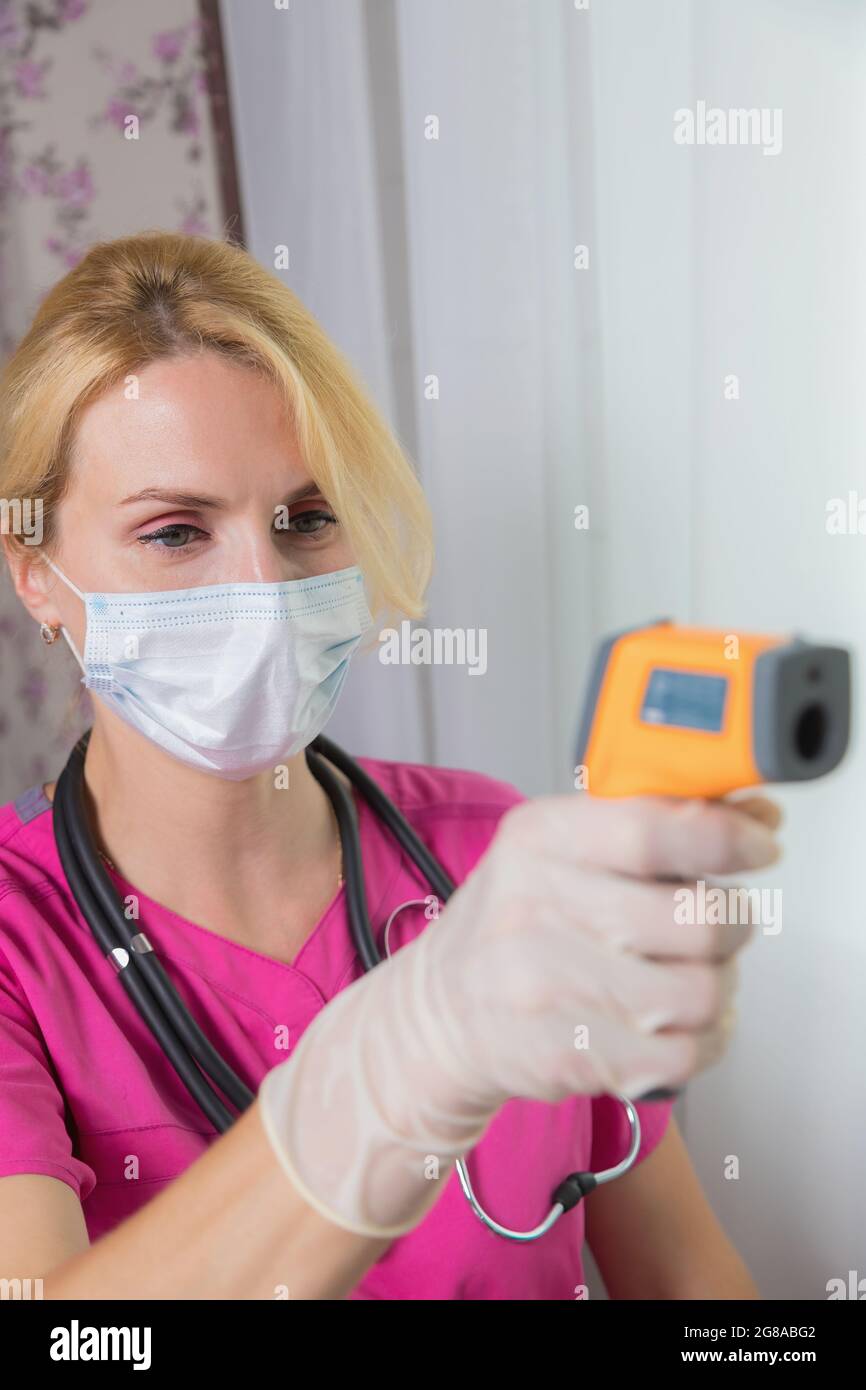 A girl doctor in a mask with an outstretched hand, a device for measuring temperature in her hand. Modern laser apparatus. Health and medicine concept Stock Photo