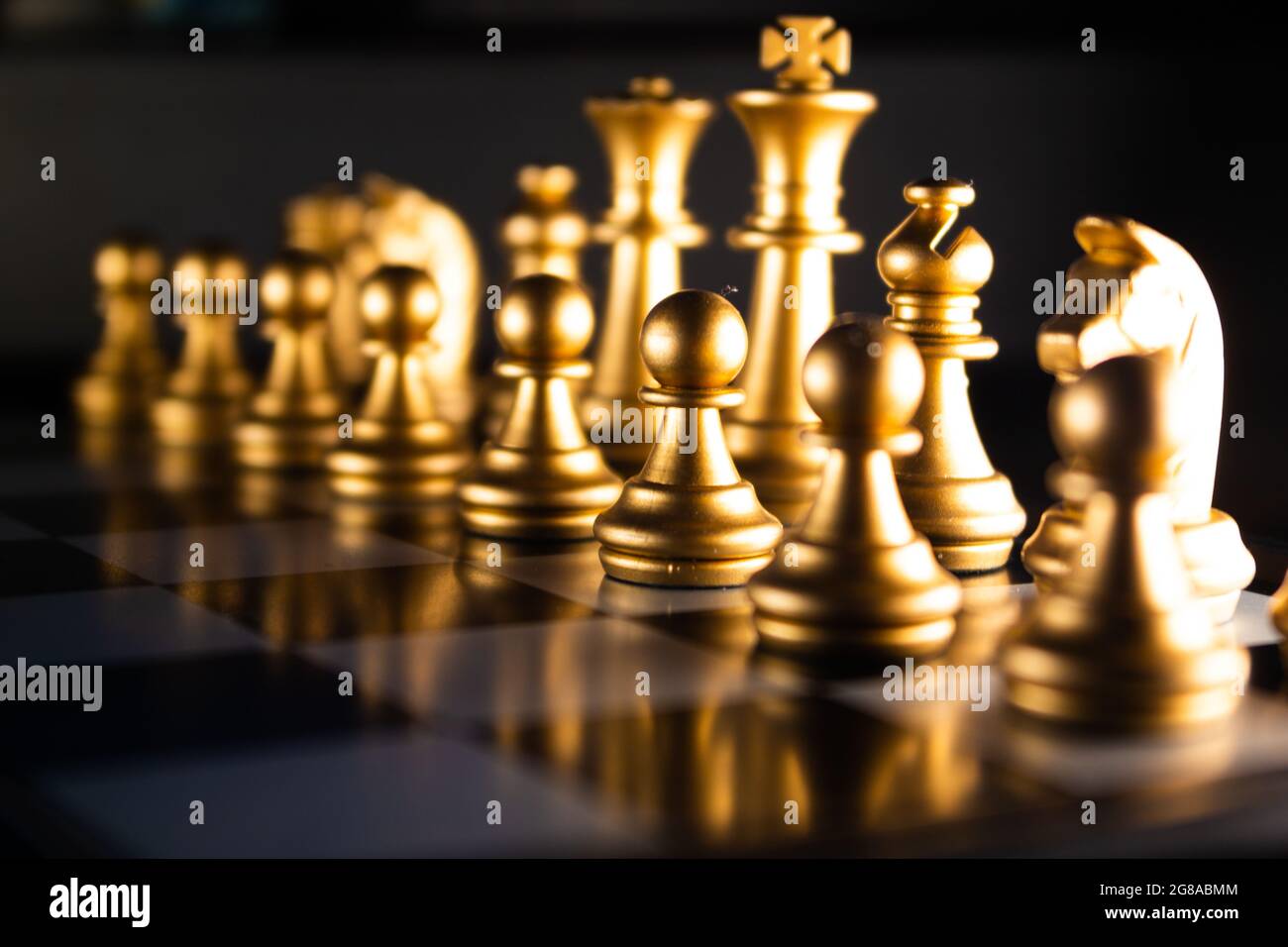 A horizontal shot of cool gold chess pieces in the starting position reflected on the board Stock Photo