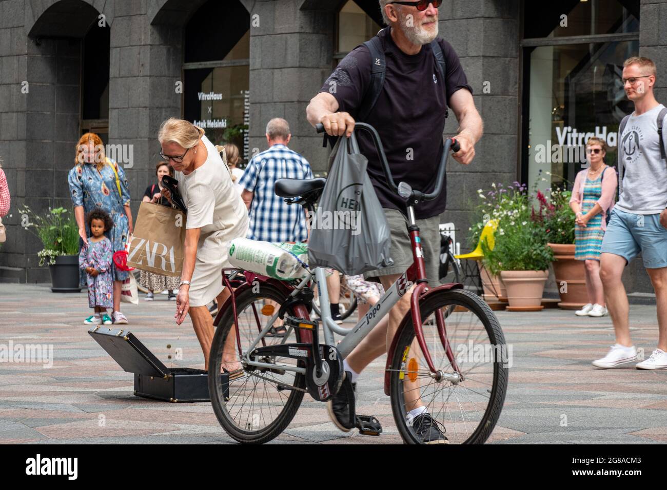 Woman dropping coins into busker's suitcase while man walks his bicycle in front. Keskuskatu, Helsinki, Finland. Stock Photo