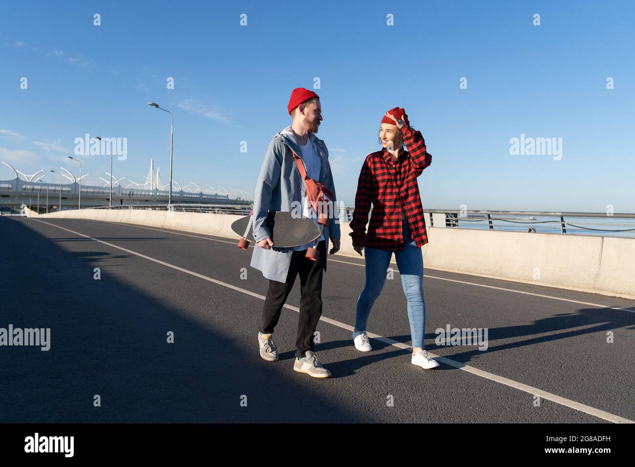 Stylish young couple of male and female walk together on bridge after longboard skating on bridge Stock Photo