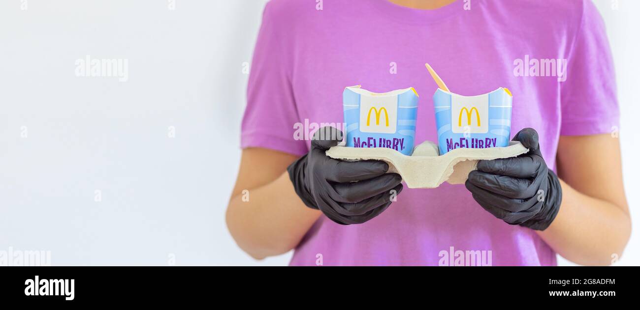 Woman in a purple t-short holding an ice cream Mcflurry in medical gloves. Delivery McCafe. fast food restaurant Mcdonalds. ake away ice cream Stock Photo
