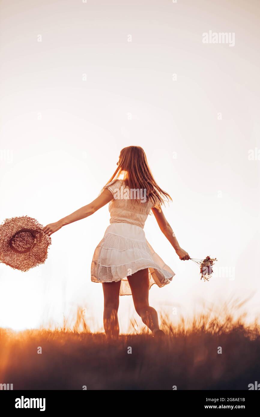 Outdoors photo of young, teen, ginger girl running through the field, holding a summer hat. Copy space Stock Photo