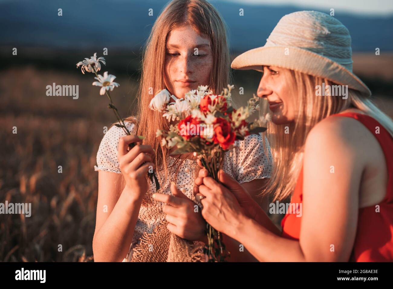 Mother and daughter smelling flowers in the field. Stock Photo