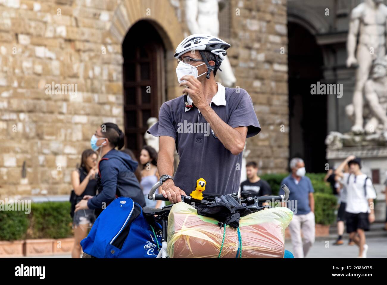 Man tourist with a bike next to Uffizi museum and David sculpture, wearing face masks during covid 19 quarantine in Italy. Slow reopening Stock Photo