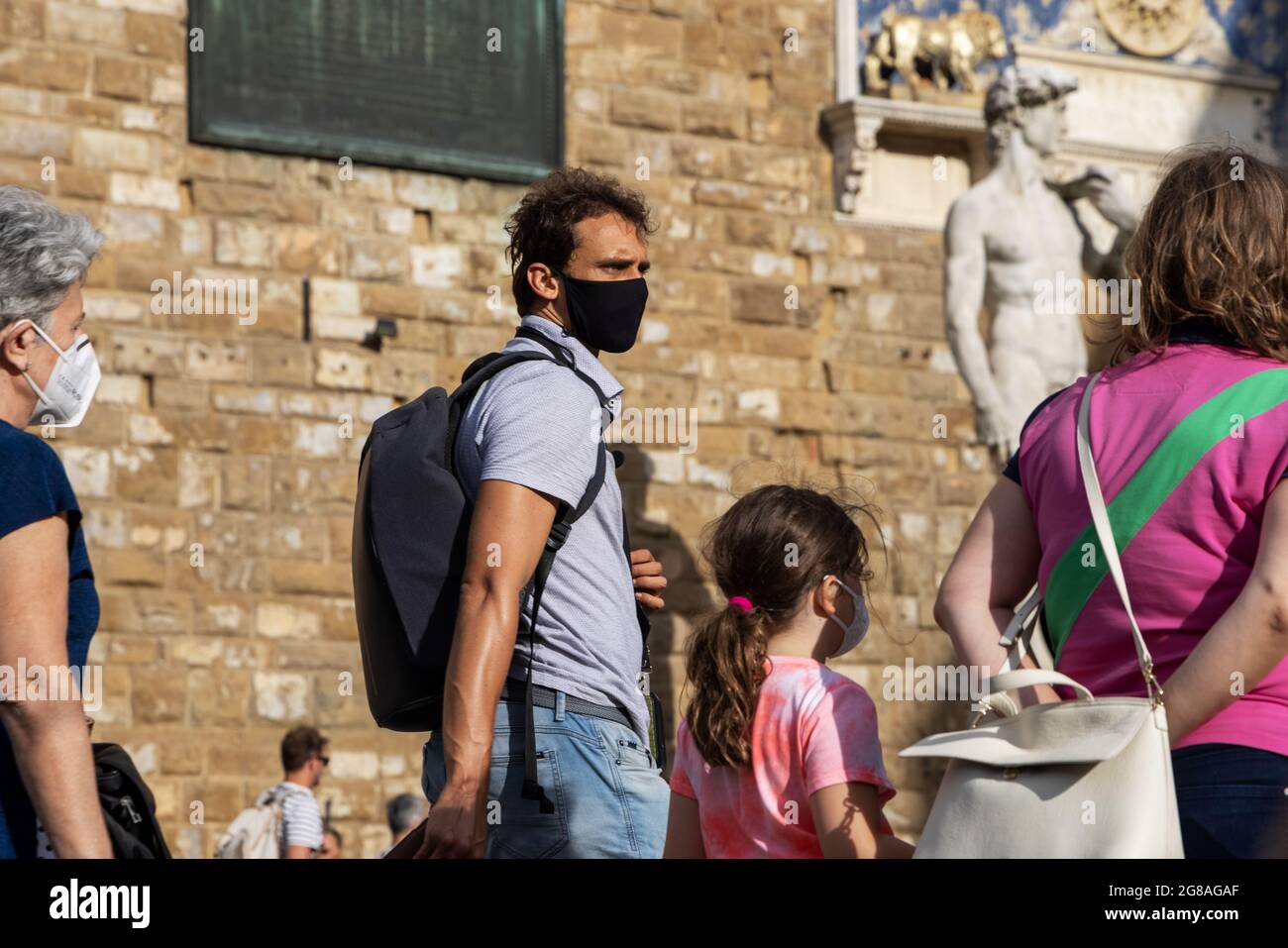 People, tourists walking in the square next to David sculpture wearing face masks during covid 19 quarantine in Italy. Slow reopening after pangemic. Stock Photo