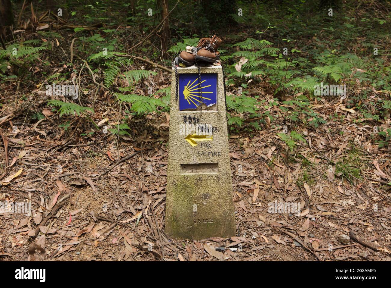 Camino de Santiago (Way of Saint James). Pilgrim boots placed on the traditional kilometre milestone of the Camino de Santiago near the town of Arzúa in Galicia, Spain. The French route and the Northern route of the Camino de Santiago go through this town shortly before both routs reach Santiago de Compostela. The scallop shell, also known as the Shell of Saint James is depicted in the milestone as a traditional symbol of the pilgrimage to Santiago de Compostela. Stock Photo