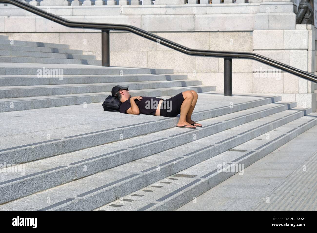 A man takes a siesta on the steps leading down to Trafalgar Sqaure on the hottest day of 2021 in the UK so far. Stock Photo