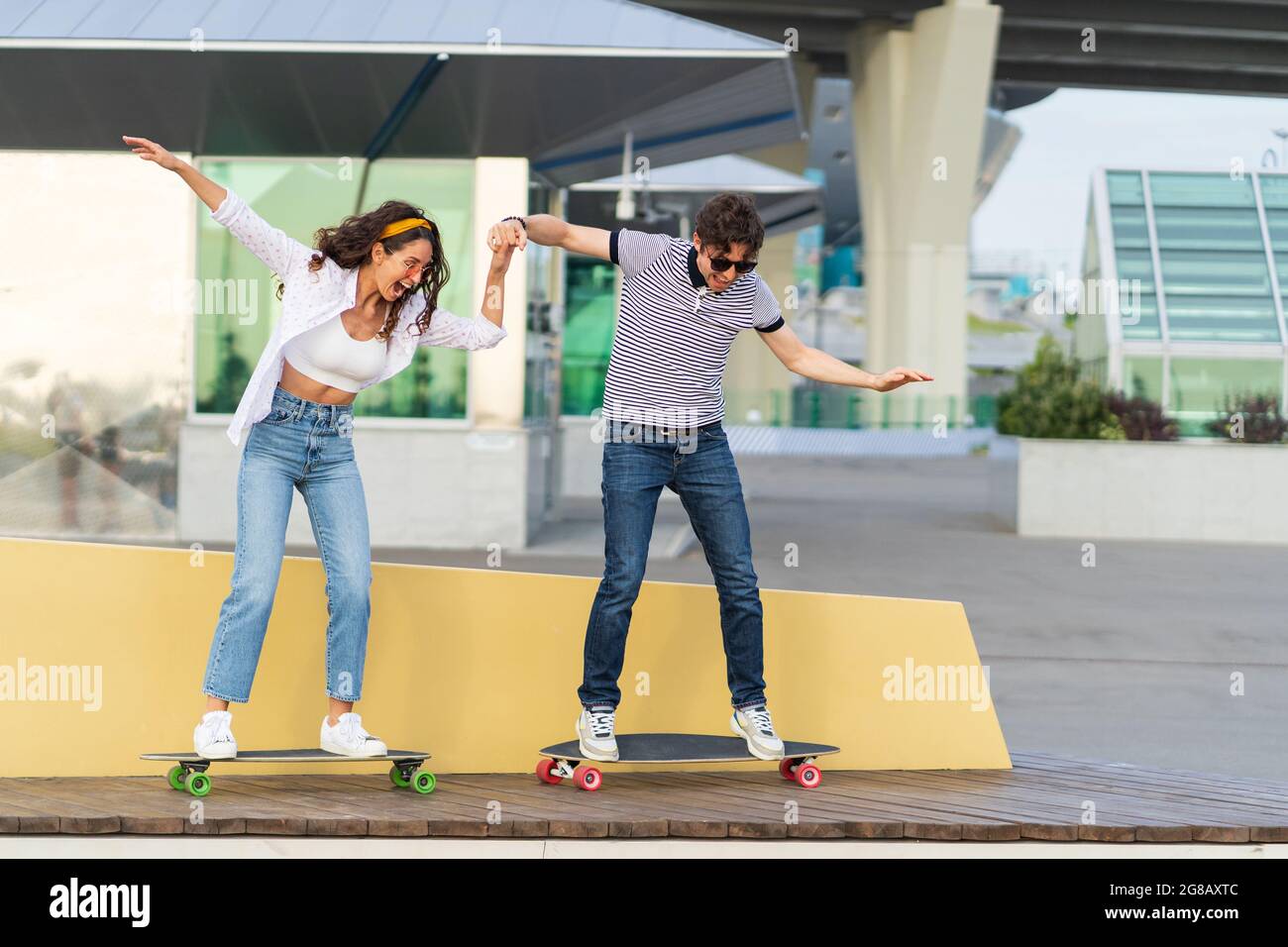 Active young skaters couple learn to ride longboard together hold hands laughing stand on skateboard Stock Photo