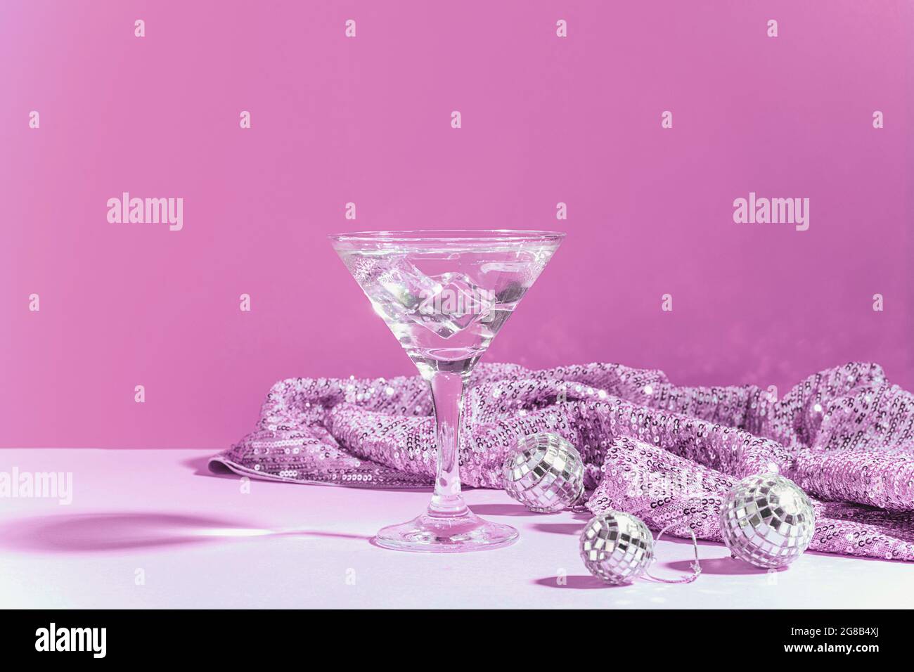 Martini with ice in an elegant glass of disco balls on a shiny pink