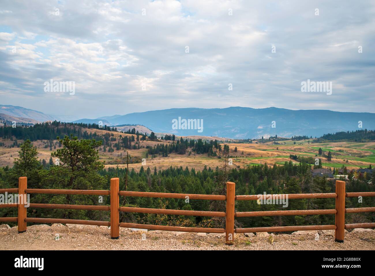 Hilly landscape behind a log hedge with mountains and forest, cloudy sky in the background Stock Photo