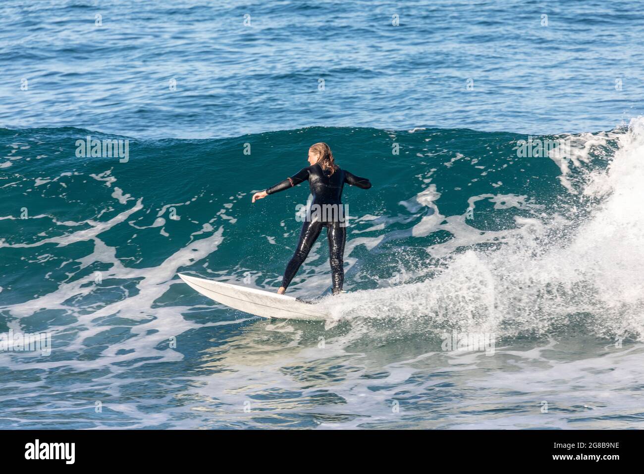 Australian teenage girl wearing a wetsuit surfing the waves at Avalon