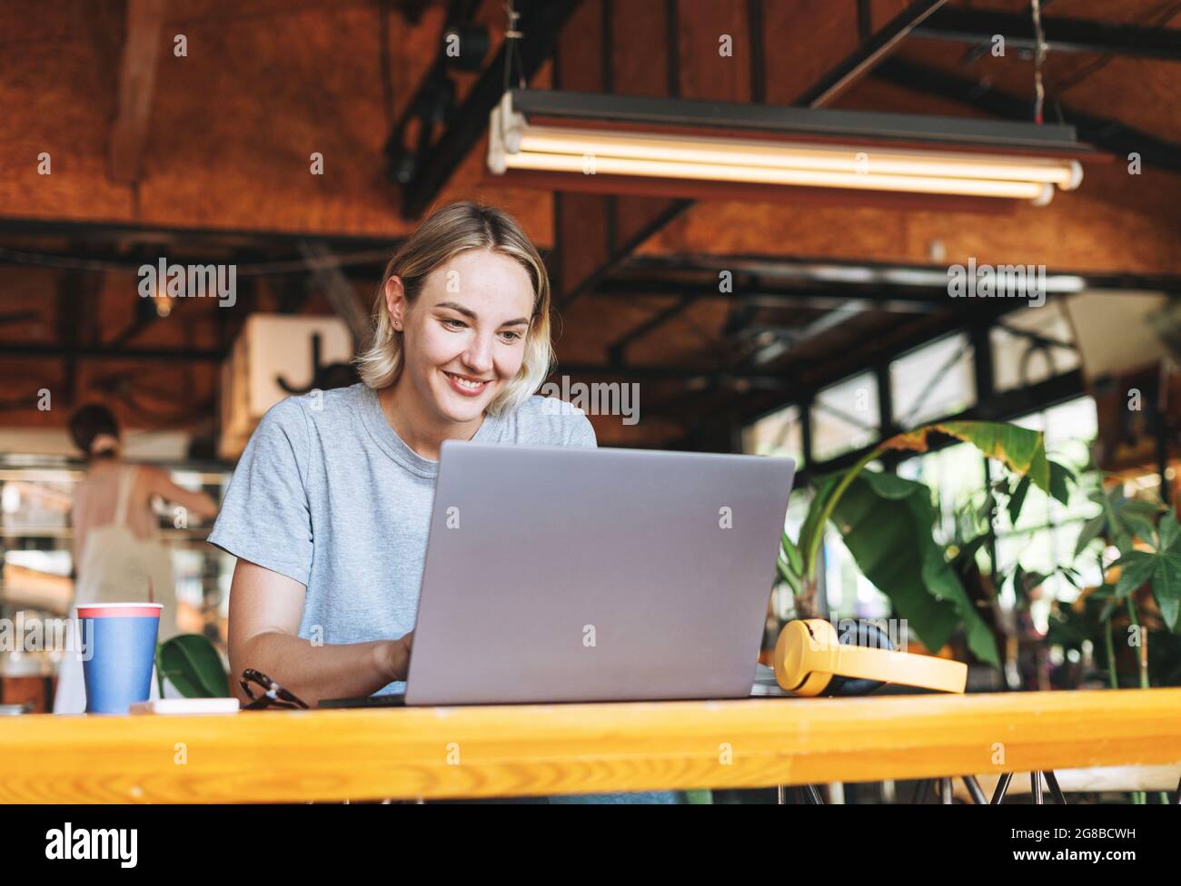Young smiling blonde woman freelancer in yellow headphones working on ...