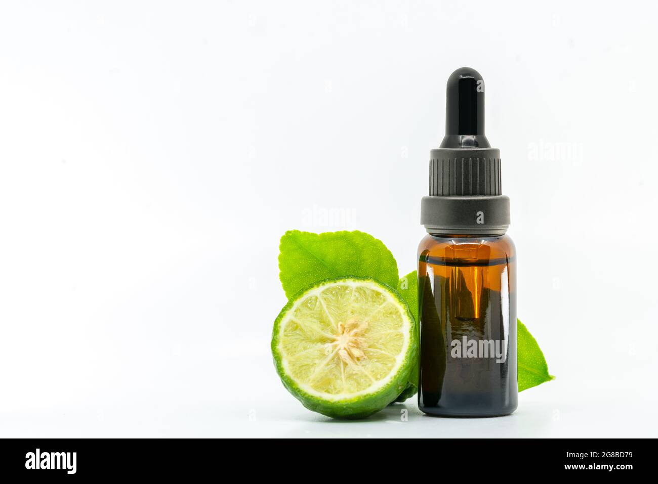 Beautiful packshot of Bergamot essential oil in a small glass bottle with fresh bergamot fruit with green leaf on white background. Blank space on the Stock Photo