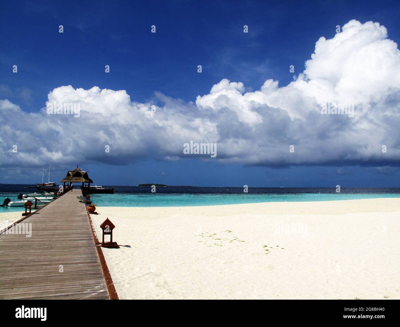Pier out to the ocean, leading to a resort's boat dock, on powdery white sand beach. Tropical vacation hideaway island on a sunny summer day. Stock Photo