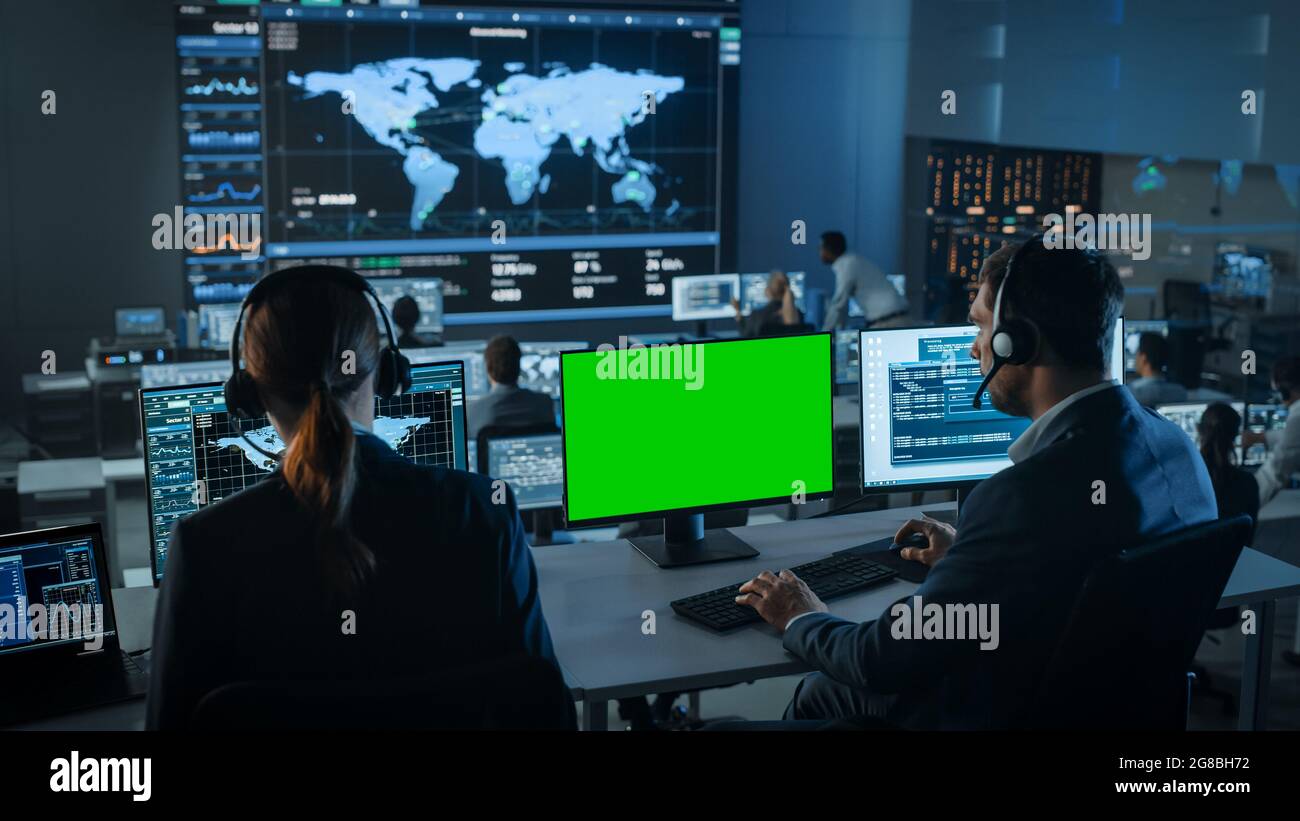 Green Screen Horizontal Mock Up on Computer Display Used by Controller in Surveillance Control Center with Global Map Tracking on a Big Digital Screen Stock Photo