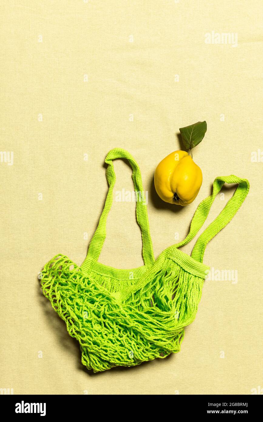 Quince apple with leaf and green mesh bag on wrinkled natural pastel colored linen background. Organic fruit has natural defects. Conscious consumeris Stock Photo