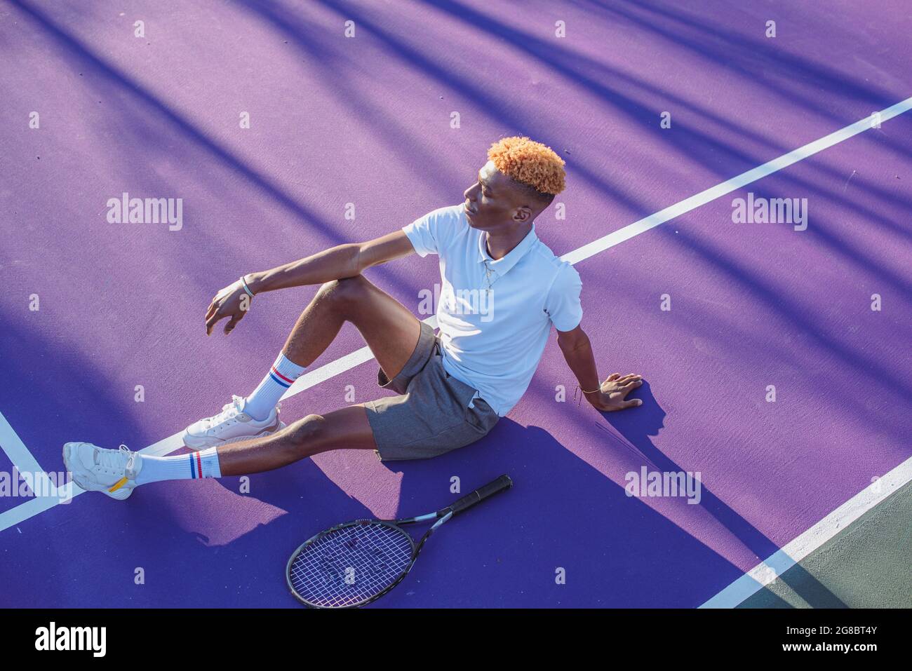 Young man resting on tennis court with racket next to him Stock Photo
