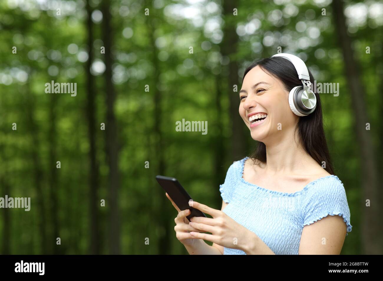 Happy asian woman laughing listening to music with wireless headphones and mobile phone in a park Stock Photo