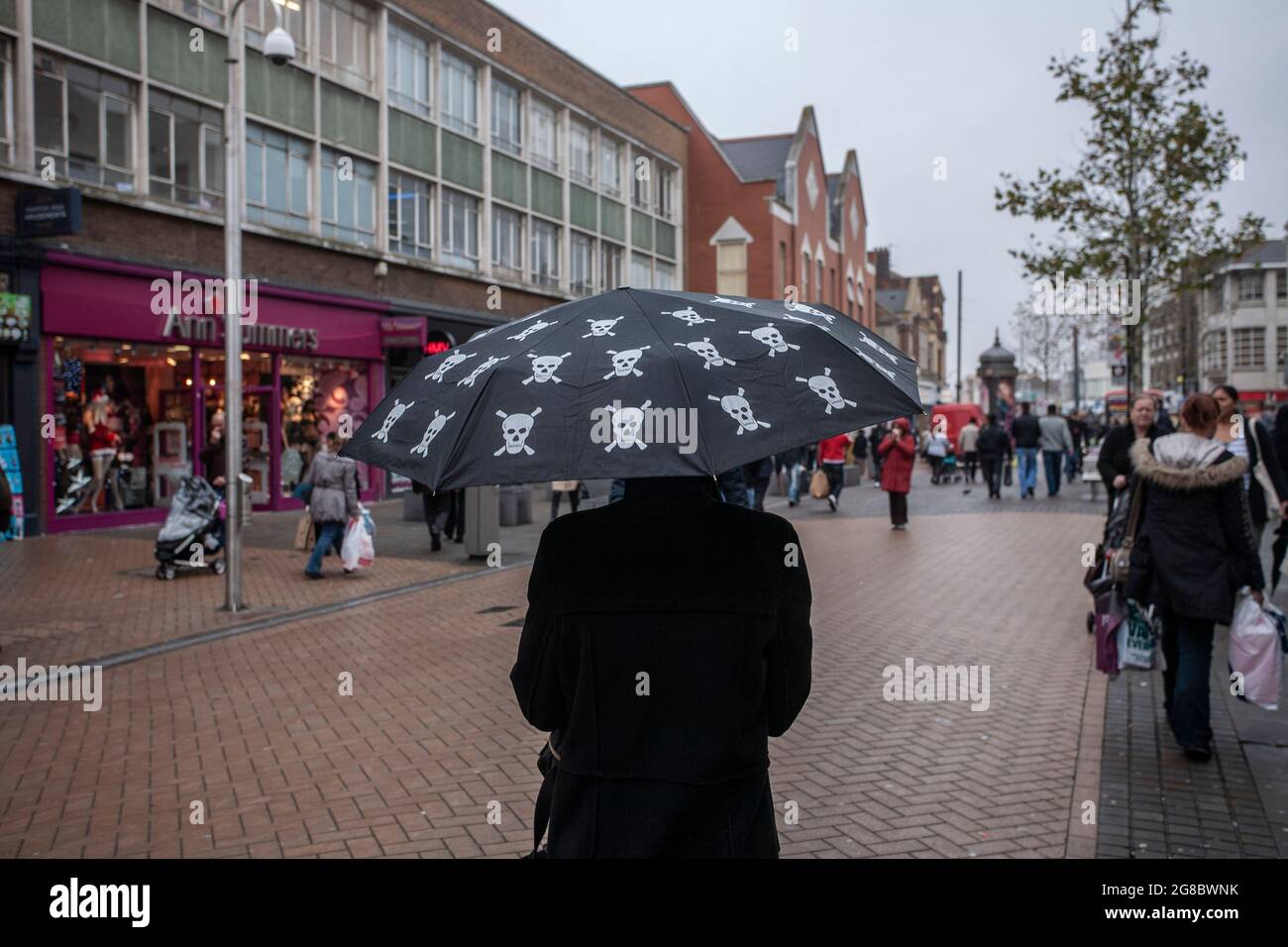 A woman walking down the high street holding an umbrella with 'Skull & Crossbones' print, as the retail sector struggles with the economy, Croydon, UK Stock Photo