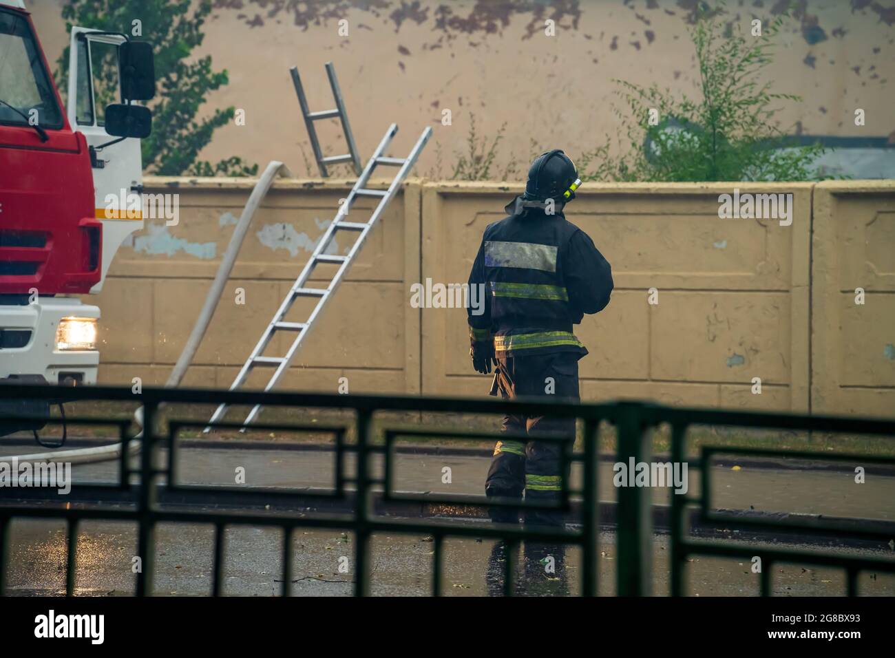 Firefighter rear view at wall with ladders and fire engine at scene of incident. Stock Photo