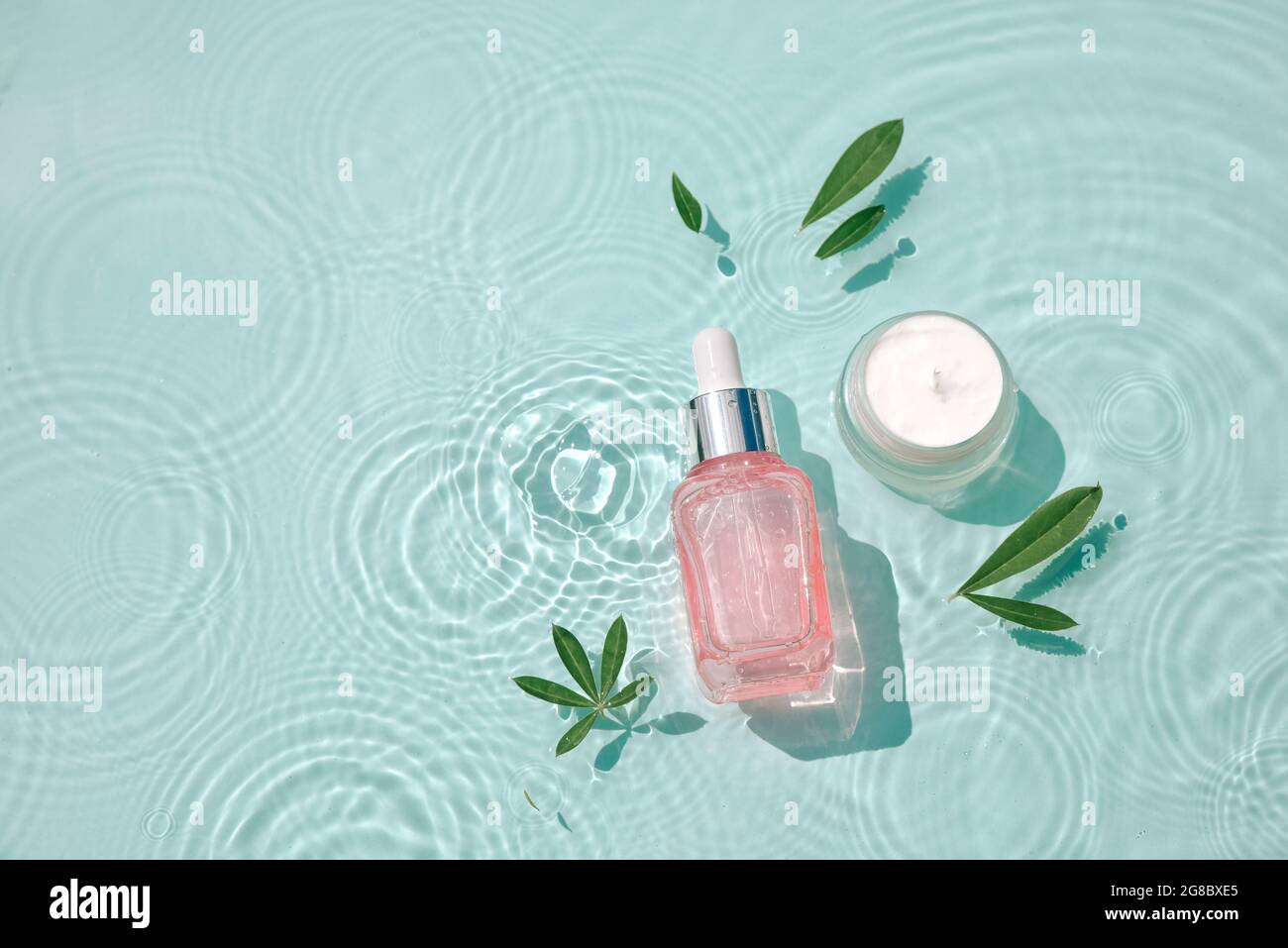 Set moisturizing cosmetic products on water with drops. Serum glass bottle and cream jar on aqua surface with waves in sunlight. Concept for advertisi Stock Photo