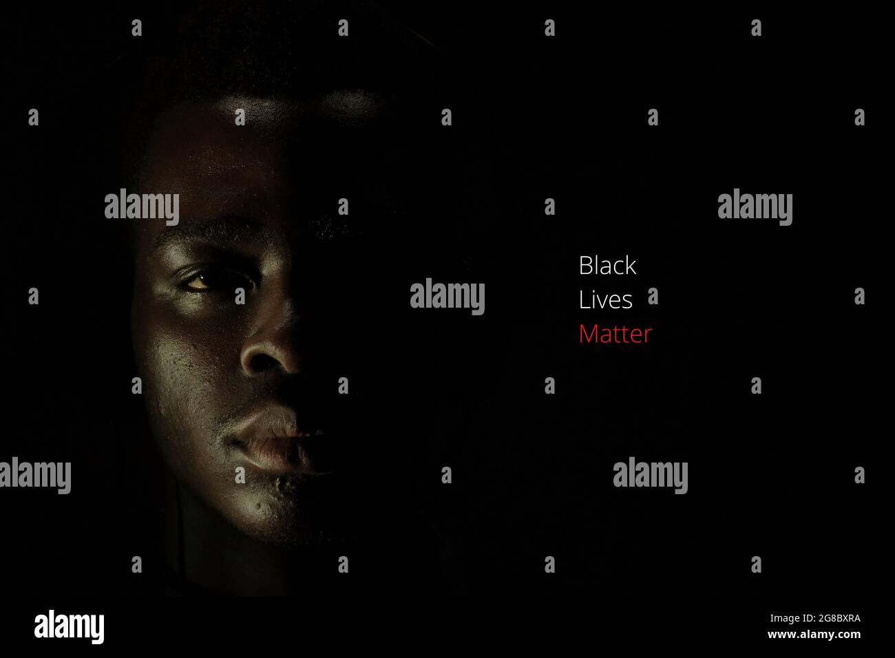 A young black African man's face is half covered in darkness, with the words Black Lives Matter in text Stock Photo