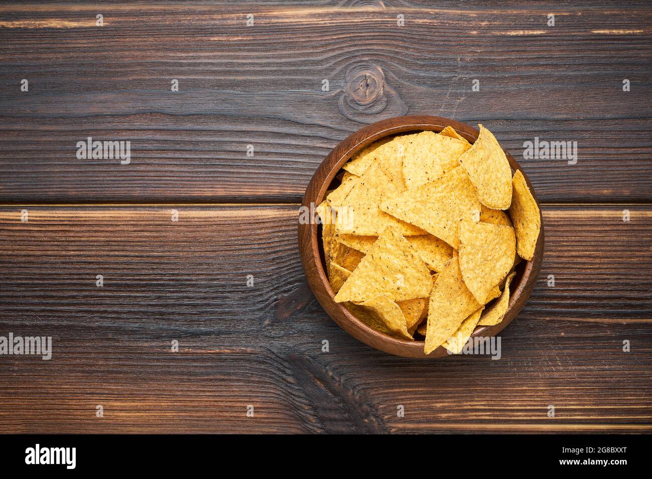 Corn tortilla chips in a wooden bowl on a dark background. Top view, copy space for text Stock Photo