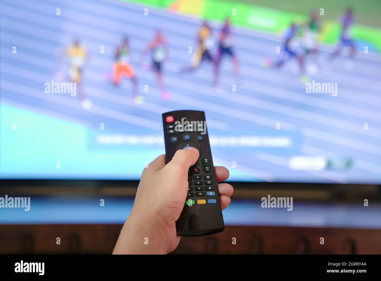 Watching sports track and field program on tv. Close up on remote control. Stock Photo