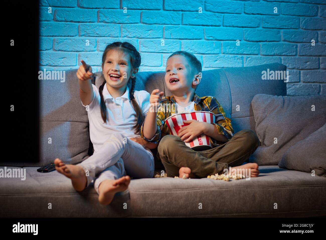 two children with remote control watching TV Stock Photo