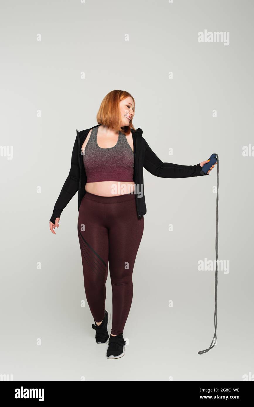 Side view of smiling body positive sportswoman holding jump rope on ...