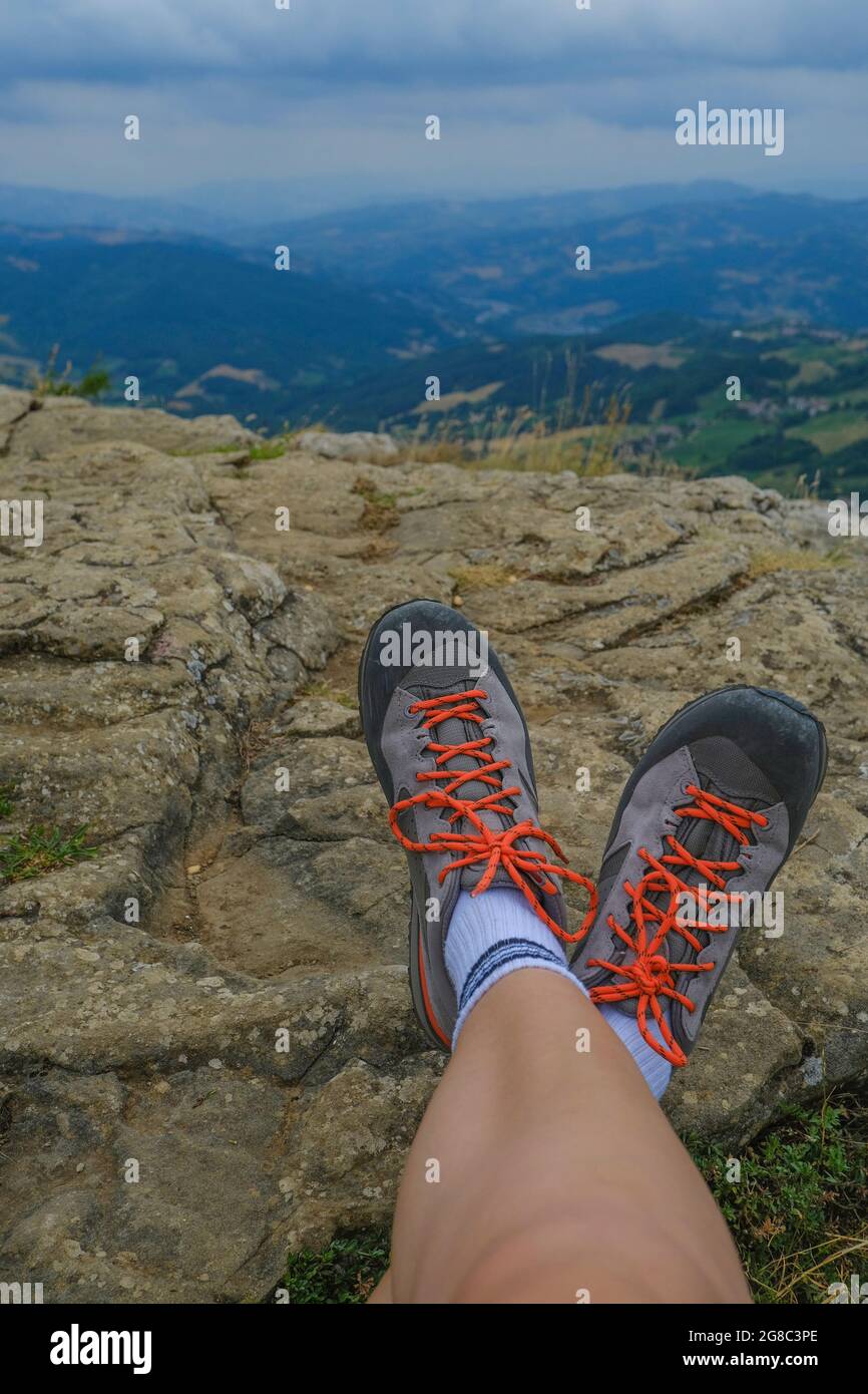 Female legs in hiking boots on the rocks across aerial mountains view and dramatic sky. Outdoor activity concept Stock Photo