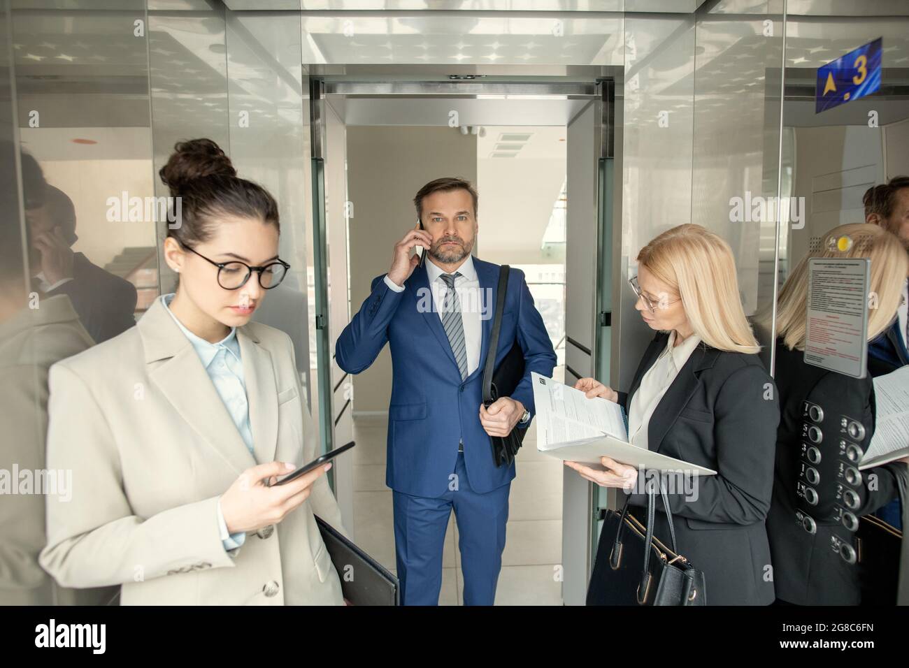 Businessman in suit talking on mobile phone while going into the elevator with other people standing in it Stock Photo
