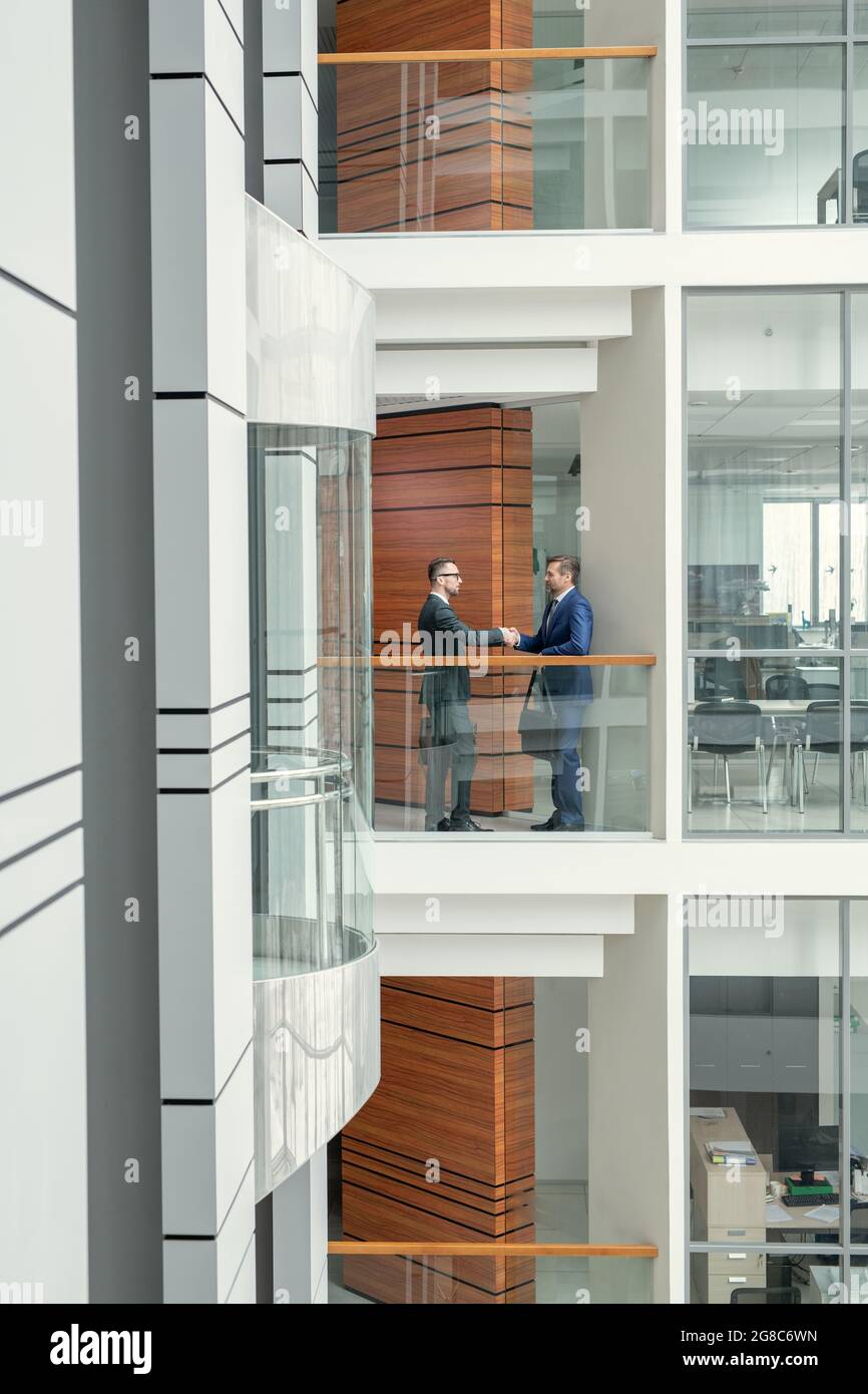 Two business men in suits shaking hands and greeting each other while standing at office corridor Stock Photo