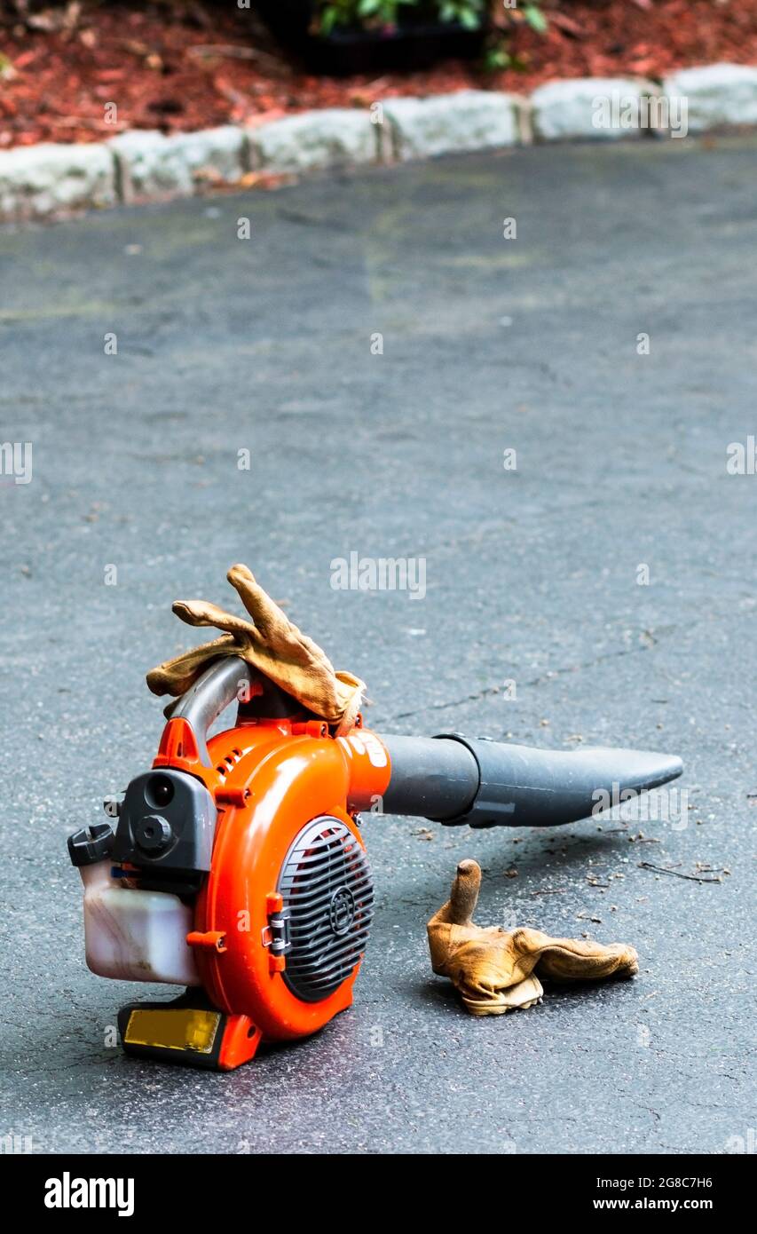 A landscapers leaf blower and gloves standing on a driveway with no people. Stock Photo