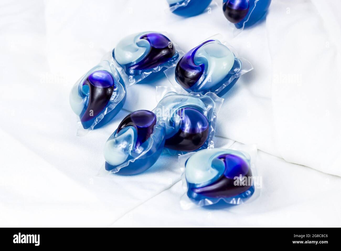 Bright blue washing pods and capsules with liquid detergent for machine laundry on white clothing background. Stock Photo