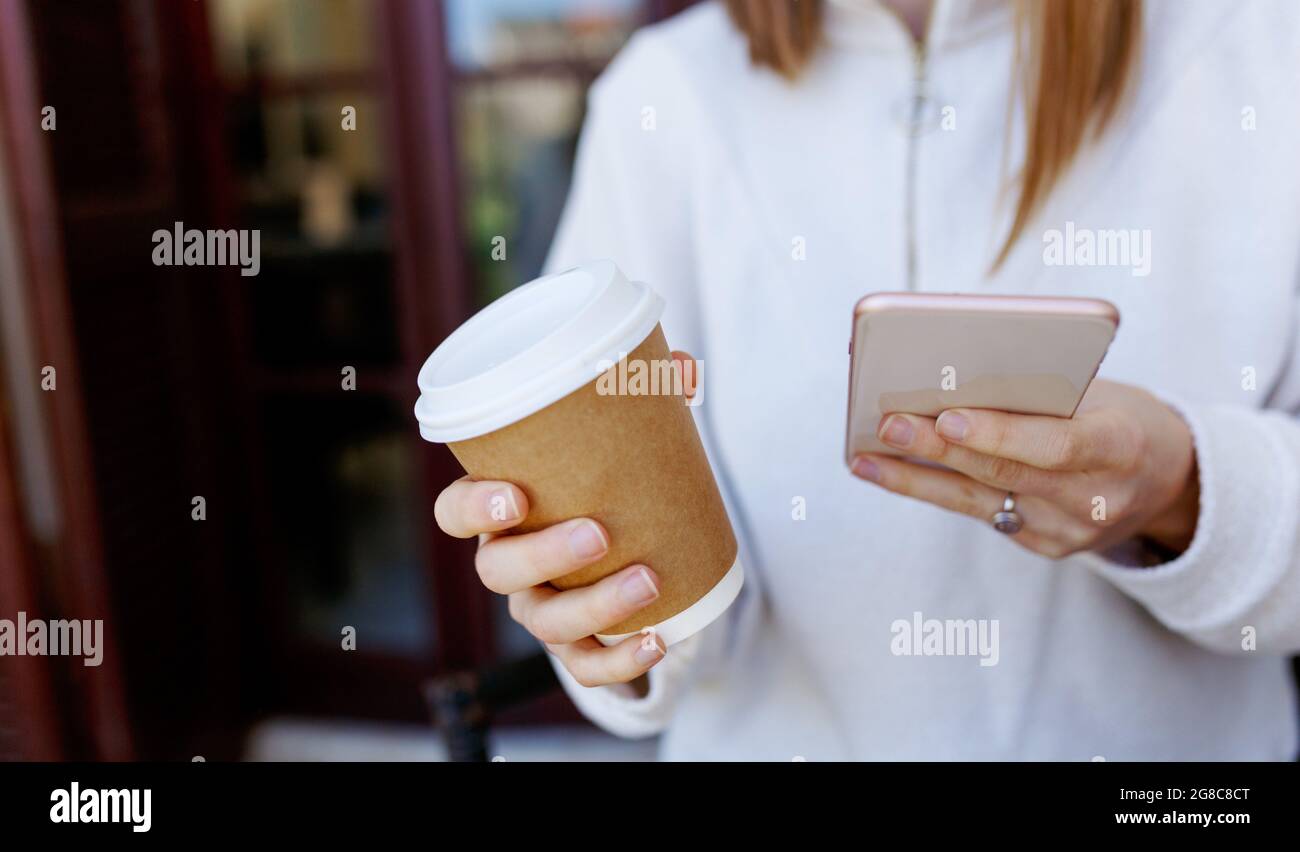 Close-up image of young hipster girl using smartphone at home interior, female hands typing on touch screen , social networking concept, coffee to go Stock Photo