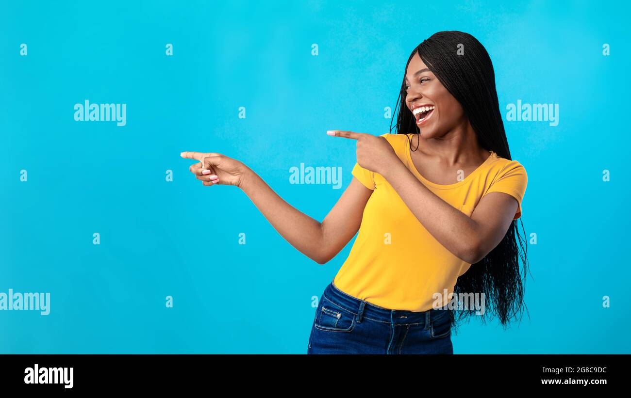 Cheerful African American Lady Pointing Fingers Aside Over Blue Background Stock Photo