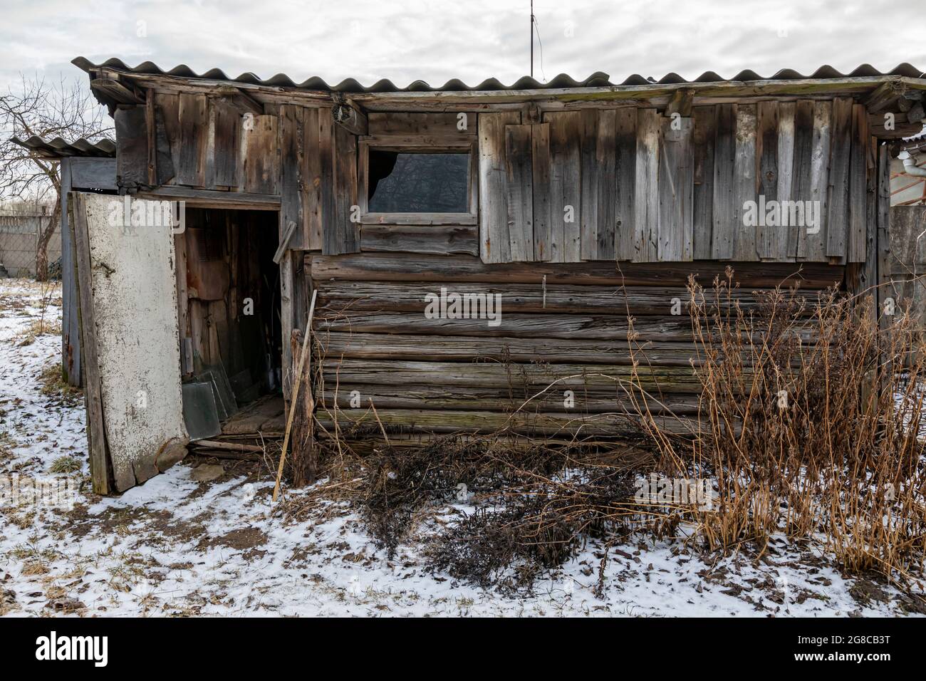 An old wooden utility shed with rotten planks. Early spring with remnants of snow on the ground. Stock Photo