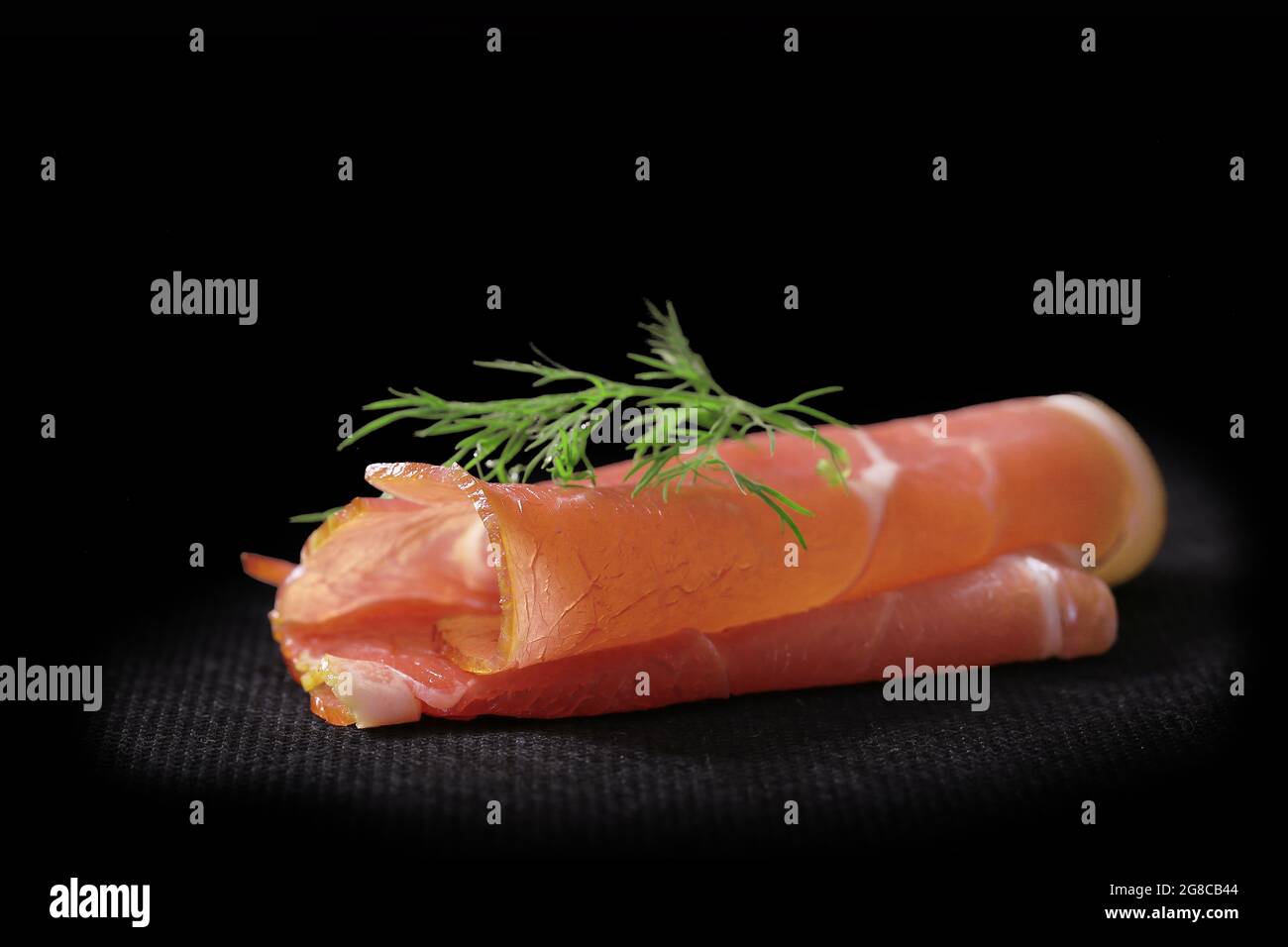 slice of dry ham rolled on a slate, isolated on black background Stock Photo