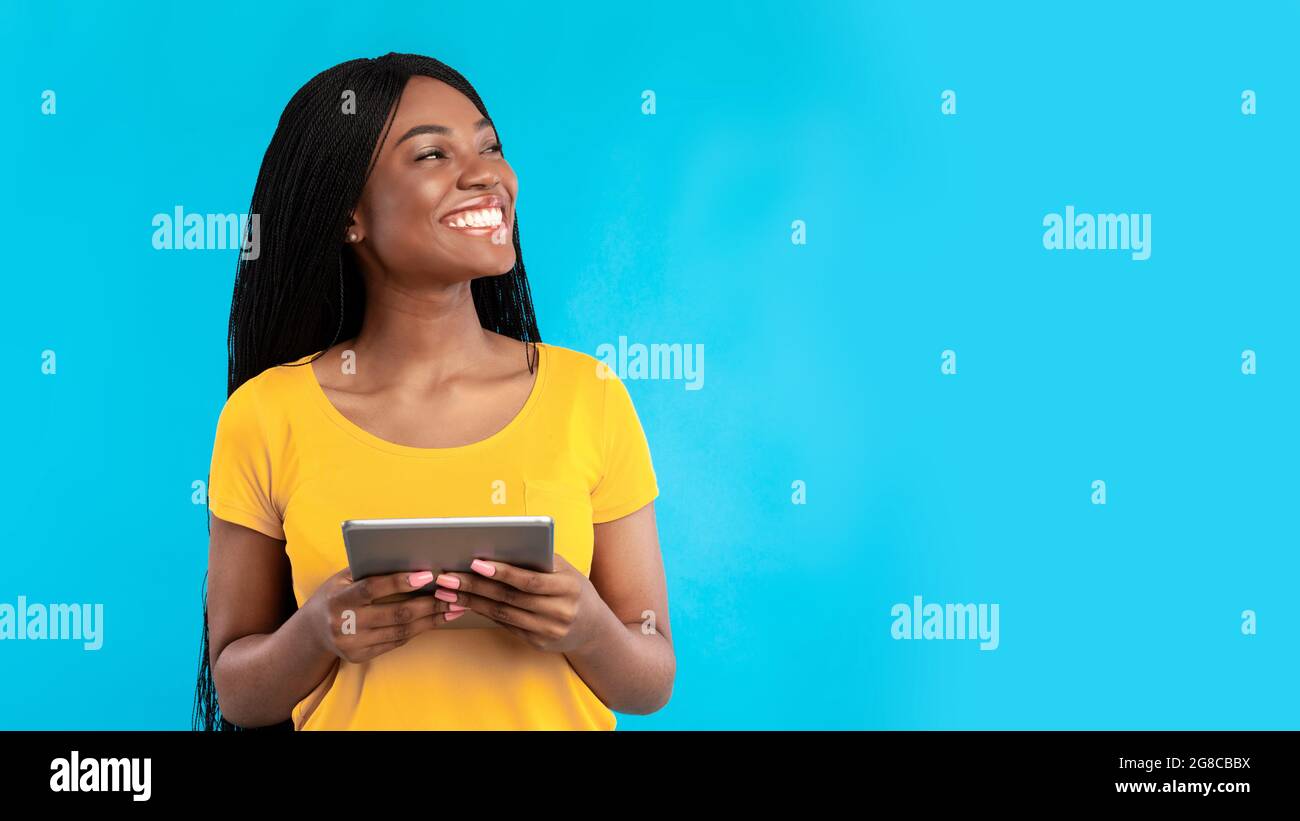 Black woman using digital tablet looking aside over blue background Stock Photo