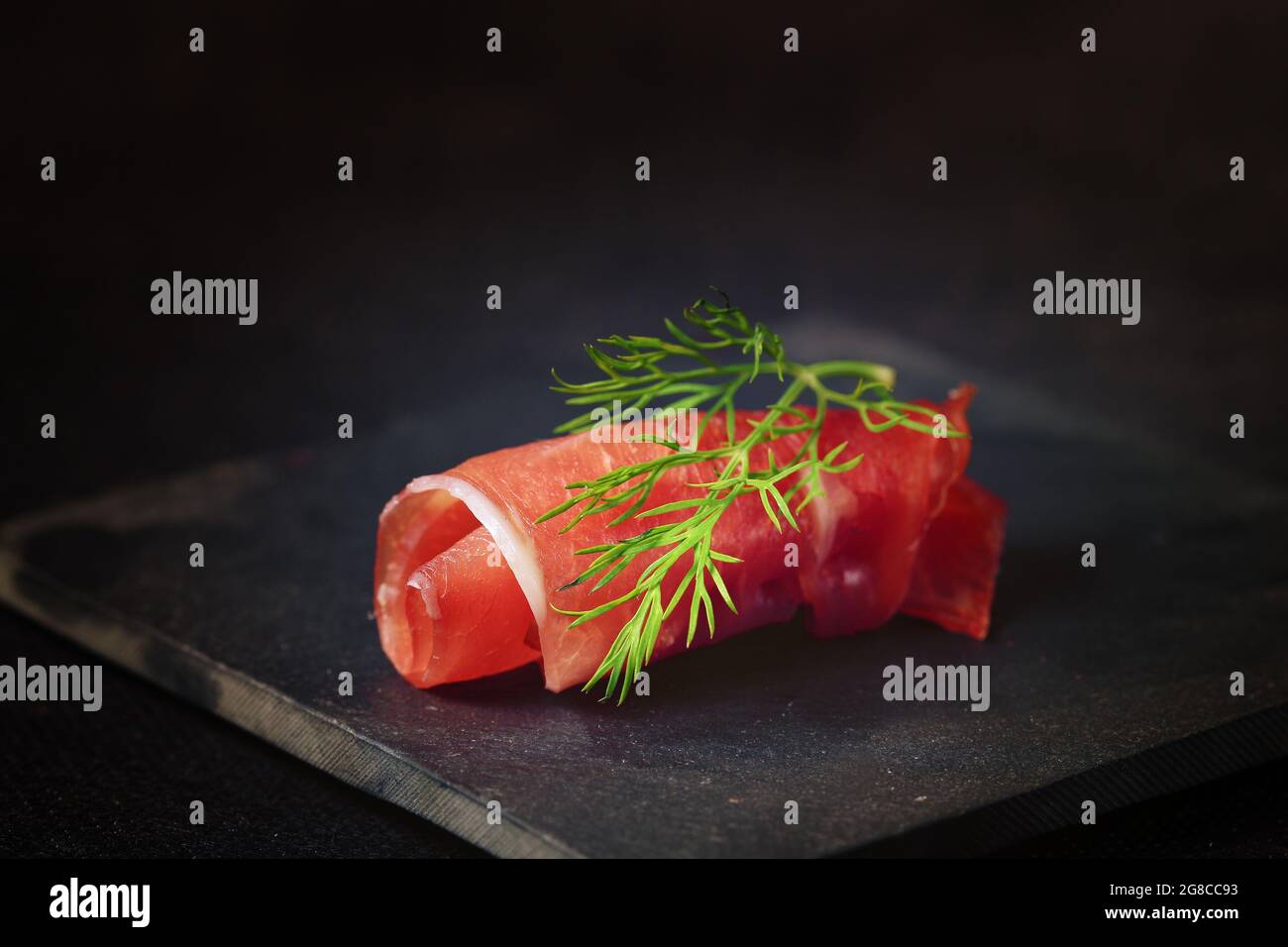 slice of dry ham rolled on a slate, isolated on black background Stock Photo