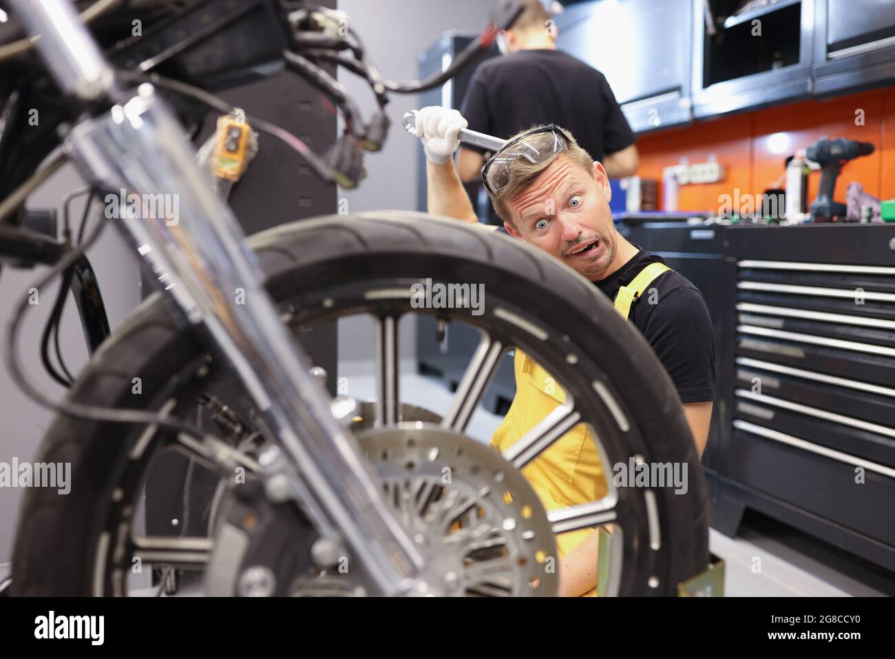 Pensive locksmith holds wrench and looks at motorcycle wheel Stock Photo