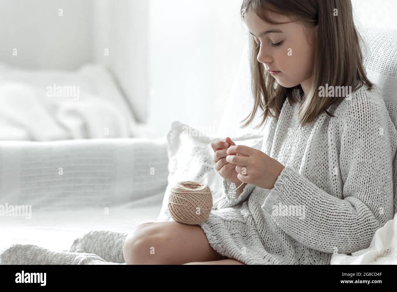 Little girl with a ball of thread and a needle at home on the couch ...