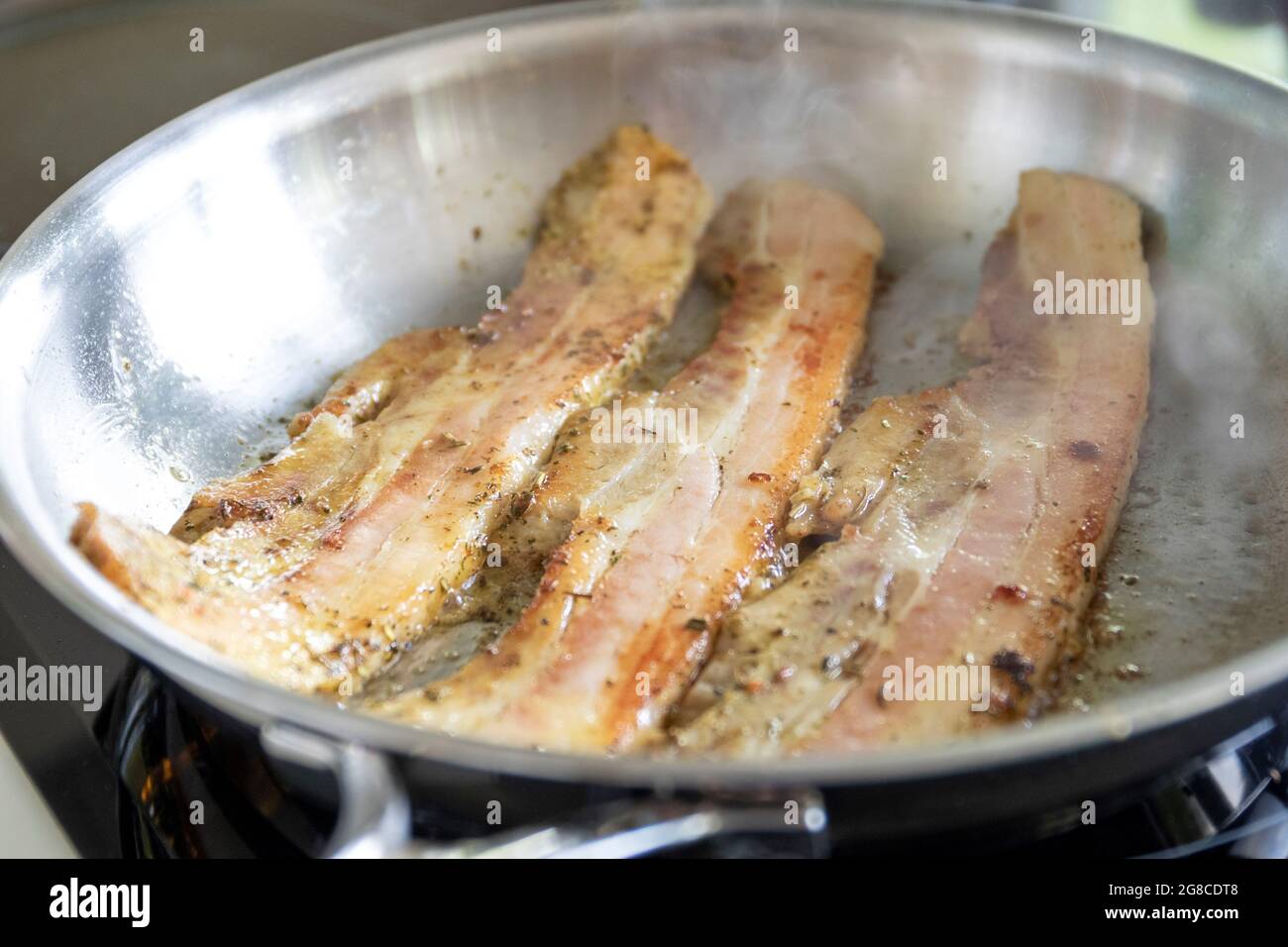 A portrait of some pork bacon strips lying in a stainless steel frying