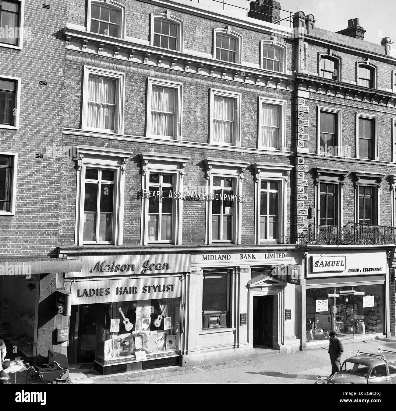 1960s, historical, a London high street of terraced victorian buildings with shops underneath, showing some of the retailers of the day; Maison Jean (Ladies Hair Stylist), Midland Bank ad Samuel (Radio & Television). All these are long gone. As is the Pearl Assurance Company Ltd (Life Assurance) whose name is shown over the first floor office windows and whose entrance is next to the hair dressers, where a pram of the era can be seen. Handwritten notice in the window of Samuel, saying 'Switch now for 625', in reference to new television sets having higher definition 625 PAL lines Stock Photo