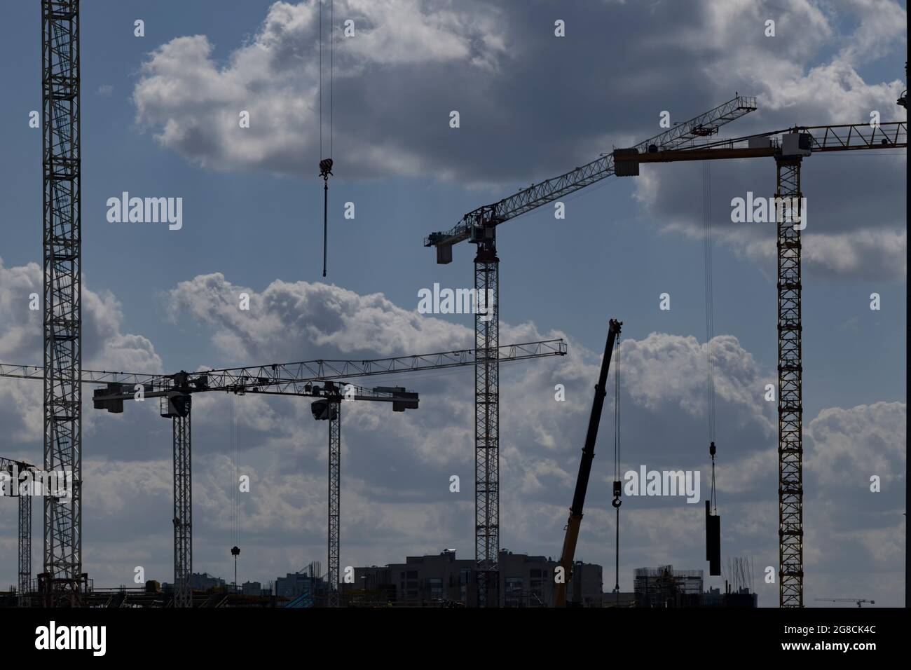 Silhouettes of a group of tower cranes against a blue sky with clouds ...