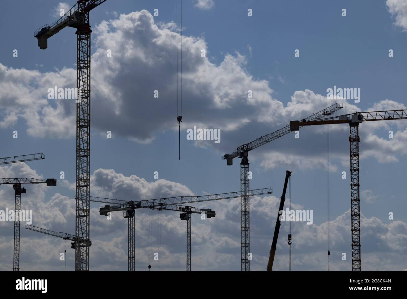 Silhouettes of a group of tower cranes against a blue sky with clouds ...